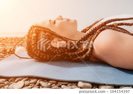 Woman sea yoga. Well looking middle aged woman with braids dreadlocks in white leggings and tops doing stretching pilates on yoga mat near sea. Female fitness yoga routine concept. Healthy lifestyle. 104154397