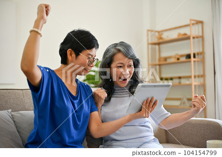 Two overjoyed retired middle-aged female besties are watching a lottery drawing online together Two overjoyed retired middle-aged female besties are watching a lottery drawing online together 104154799