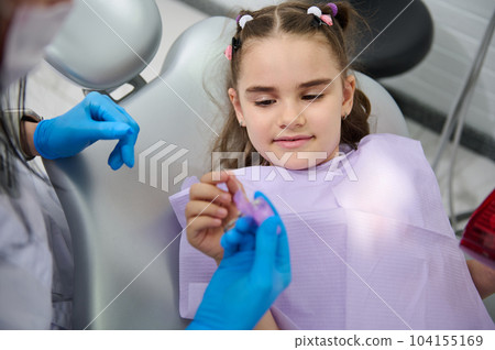 Close-up portrait of a beautiful Middle-Eastern little child girl at dentist's appointment, holding dental floss, getting teeth check-up in pediatric dentistry clinic. Dental care and hygiene concept Close-up portrait of a beautiful Middle-Eastern little child girl at dentist's appointment, holding dental floss, getting teeth check-up in pediatric dentistry clinic. Dental care and hygiene concept 104155169