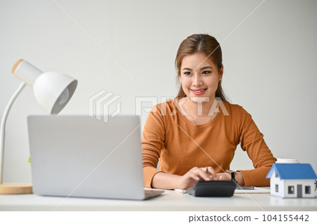 A beautiful Asian woman using a calculator to calculate her house loan at her desk. 104155442