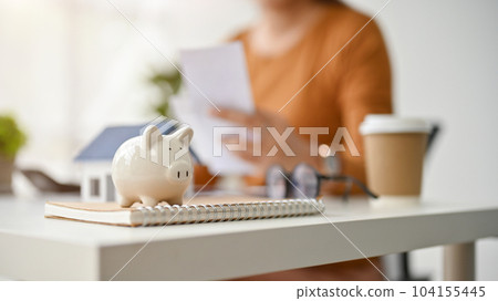 Close-up image of a piggy bank is on table with a female real estate agent working behind. Close-up image of a piggy bank is on table with a female real estate agent working behind. 104155445