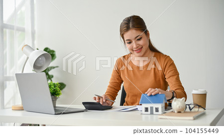 A female real estate agent working at her desk, calculating the down payment 104155449