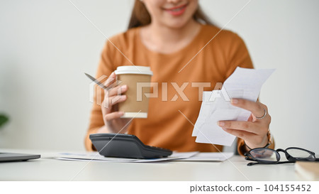 Close-up image of a beautiful Asian woman sipping coffee and checking her bills 104155452