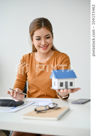 A female real estate agent holding and looking at a house model at her desk. A female real estate agent holding and looking at a house model at her desk. 104155462