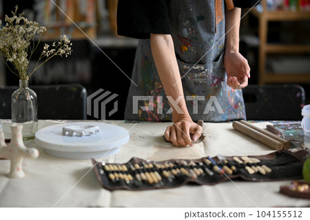 Close-up image of a male artist potter kneading raw clay at his worktable in his pottery studio. Close-up image of a male artist potter kneading raw clay at his worktable in his pottery studio. 104155512