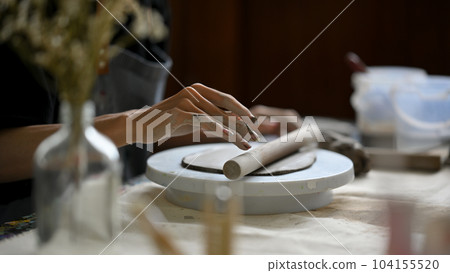Close-up image of a male artist kneading raw clay with a clay roller on a pottery wheel 104155520