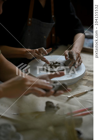 Close-up hands image, A man making a handmade clay ornament in a workshop with his friend. 104155532