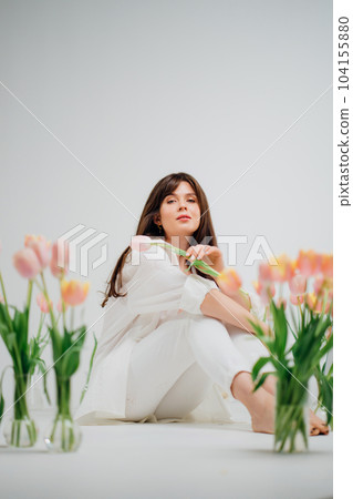 gentle brunette in white sits on the floor with vases of tulips gentle brunette in white sits on the floor with vases of tulips 104155880