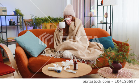 Sick ill woman suffering from cold or allergy sitting on home sofa sneezes wipes snot into napkin 104156697