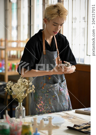 A man focuses making earthenware or sculpting an ornament with raw clay 104157051