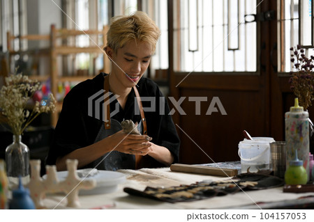 A happy man enjoys making earthenware, kneading raw clay to sculpt an ornament A happy man enjoys making earthenware, kneading raw clay to sculpt an ornament 104157053