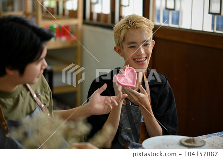 A happy Asian gay man shows his painted ceramic plate, enjoying a handicraft workshop A happy Asian gay man shows his painted ceramic plate, enjoying a handicraft workshop 104157087