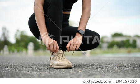 Close-up image of a sporty woman in sportswear tying her running shoelaces on the street 104157520
