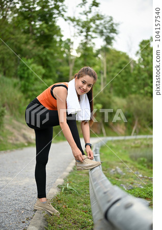 A sporty Asian woman in sportswear gets ready and ties her running shoelaces on the street A sporty Asian woman in sportswear gets ready and ties her running shoelaces on the street 104157540
