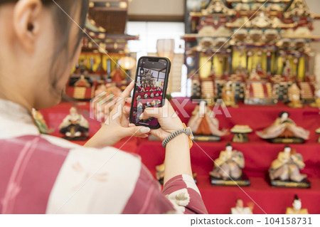 A young woman taking a picture of the Hina dolls displayed at the inn with her smartphone Image of a girls' trip 104158731