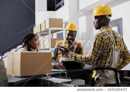 African american warehouse workers talking with stock supply manager at reception desk. Woman supervisor checking goods inventory in storehouse and taking notes on clipboard 104160437