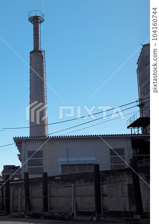 A factory chimney rises in the blue sky A factory chimney rises in the blue sky 104160744