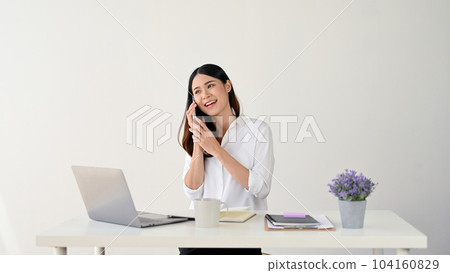 An attractive Asian businesswoman is talking on the phone with a client at her desk. 104160829