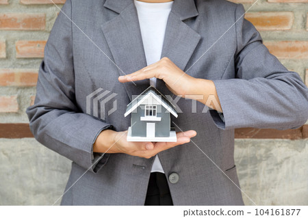 Real estate agent hands holding the home model stand in front of the red brick wall background or Sales presenting home insurance 104161877