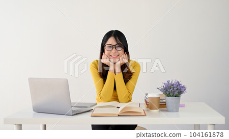 A pretty Asian female college student is smiling at the camera, hands on her chin 104161878