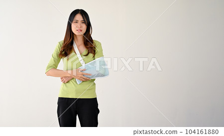 A sad and painful young Asian woman with her accidentally broken arm in an arm sling 104161880