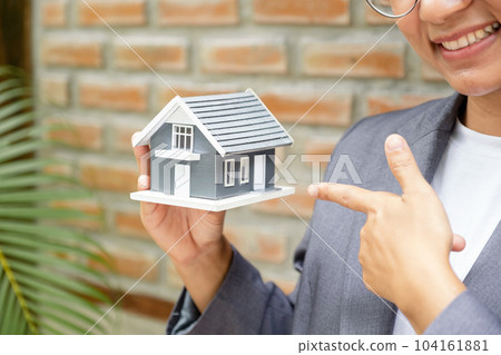 Real estate agent hands holding the home model stand in front of the red brick wall background or Sales presenting home insurance 104161881