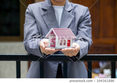 Real estate agent hands holding the home model stand in front of the home wall background 104161886