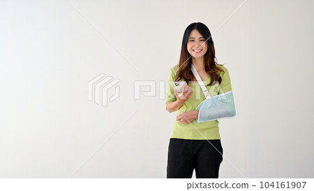 A woman wearing an arm sling to support her injured arm, and holding her smartphone. A woman wearing an arm sling to support her injured arm, and holding her smartphone. 104161907