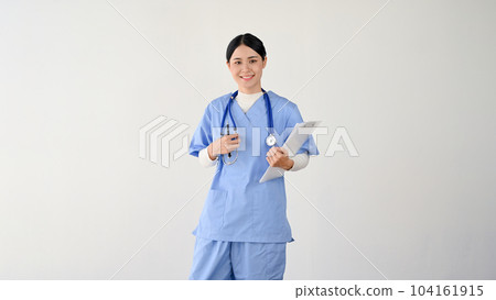 A female doctor in scrubs is holding a clipboard while standing against an isolated white background. 104161915