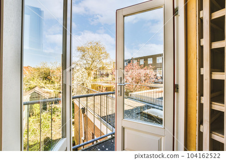 a view from the inside of a house through an open door to a balcony with trees and buildings in the background 104162522