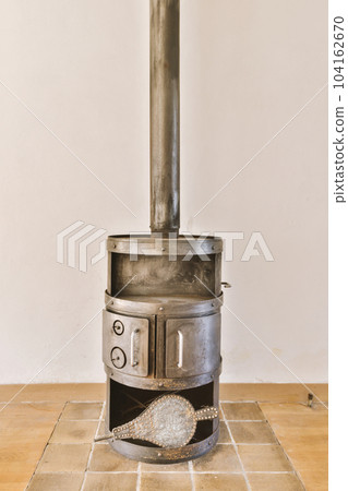 a wood burning stove in the corner of a room with tile floor and white wall behind it is an open door a wood burning stove in the corner of a room with tile floor and white wall behind it is an open door 104162670