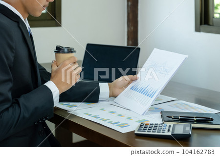 Businessman hand holding coffee cup, analysis the graph with laptop at the home office for setting challenging business goals And planning to achieve the new target Businessman hand holding coffee cup, analysis the graph with laptop at the home office for setting challenging business goals And planning to achieve the new target 104162783