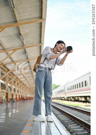 A female backpacker taking a photo with her camera at the railway station. A female backpacker taking a photo with her camera at the railway station. 104163387