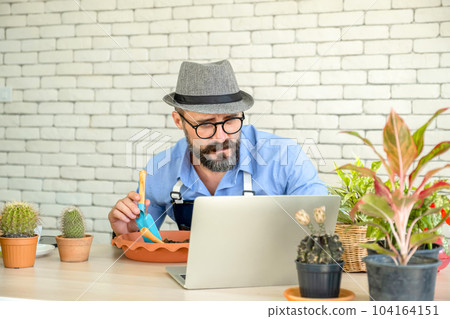 Hipster elderly men learn to take care of plants online with laptop, a hobby of urban home gardening after sustainable retirement 104164151