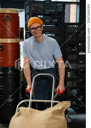 Roastery worker standing with sacks with coffee beans uploading. Roastery worker standing with sacks with coffee beans uploading. 104164884