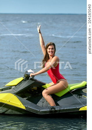Sporty Caucasian woman driving water bike on summer sunny day, enjoying active rest, raising arm. 104165040