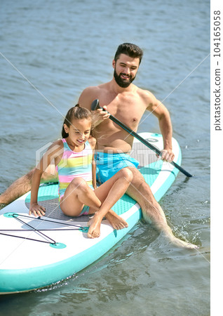 Man with daughter sitting on surfboard in water enjoying summertime spending time together at resort Man with daughter sitting on surfboard in water enjoying summertime spending time together at resort 104165058
