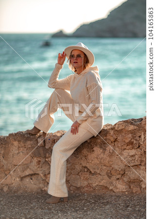 Happy blonde woman in a white suit and hat posing at the camera against the backdrop of the sea Happy blonde woman in a white suit and hat posing at the camera against the backdrop of the sea 104165863