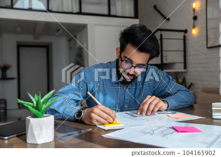 Dark-haired young man sitting at the table and preparing a project draft 104165902