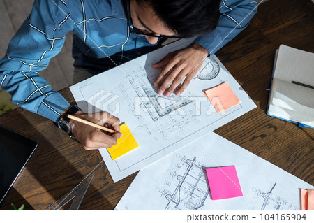 Dark-haired young man sitting at the table and preparing a project draft Dark-haired young man sitting at the table and preparing a project draft 104165904