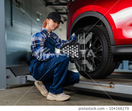 A female auto mechanic makes a camber. Woman working in a car service. 104166279