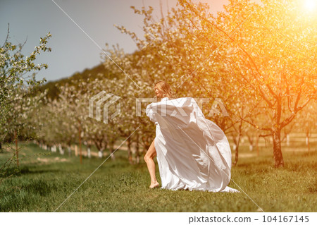 Woman white dress park. A woman in a white dress runs through a blossoming cherry orchard. The long dress flies to the sides, the bride runs rejoicing in life. Woman white dress park. A woman in a white dress runs through a blossoming cherry orchard. The long dress flies to the sides, the bride runs rejoicing in life. 104167145
