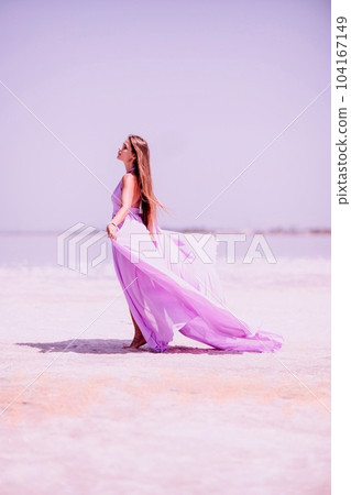 Woman pink salt lake. Against the backdrop of a pink salt lake, a woman in a long pink dress takes a leisurely stroll along the white, salty shore, capturing a wanderlust moment. 104167149