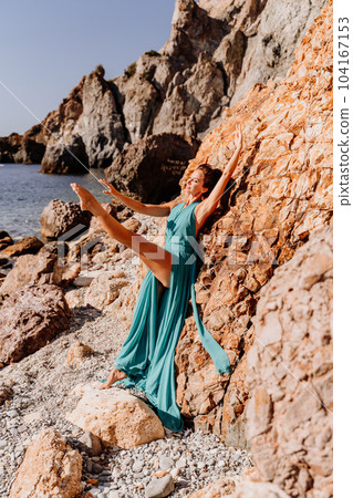 Woman green dress sea. Woman in a long mint dress posing on a beach with rocks on sunny day. Girl on the nature on blue sky background. Woman green dress sea. Woman in a long mint dress posing on a beach with rocks on sunny day. Girl on the nature on blue sky background. 104167153