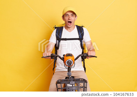 Fast transport express home delivery. Online order. Delivery man in cap with thermo backpack on electric scooter positing isolated on yellow background. Fast transport express home delivery. Online order. Delivery man in cap with thermo backpack on electric scooter positing isolated on yellow background. 104167633