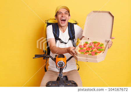 Portrait of funny crazy courier man holding pizza in carton boxes, wearing white T-shirt, riding electric scooter, posing against yellow wall, laughing put loud, mixing orders. Portrait of funny crazy courier man holding pizza in carton boxes, wearing white T-shirt, riding electric scooter, posing against yellow wall, laughing put loud, mixing orders. 104167672