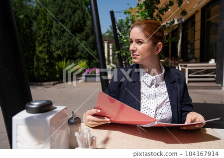 Portrait of a business woman looking at a menu in a cafe outdoors. 104167914
