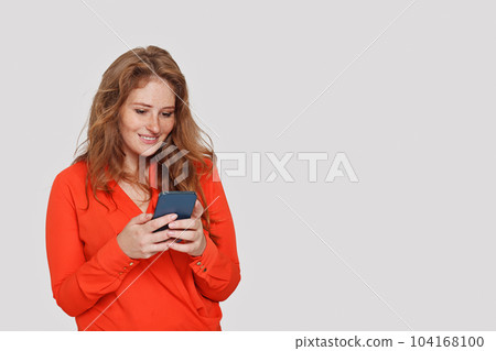 Attractive cheerful woman texting by phone on white studio wall background 104168100