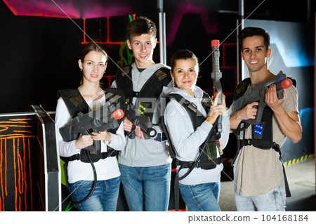 Four happy young men an women posing with laser pistols in their hands in dark laser tag room 104168184