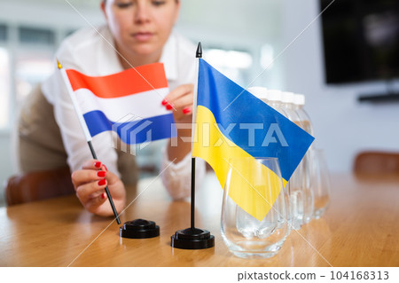 Unrecognizable girl sets midget flags of Ukraine and Netherlands before international negotiations 104168313